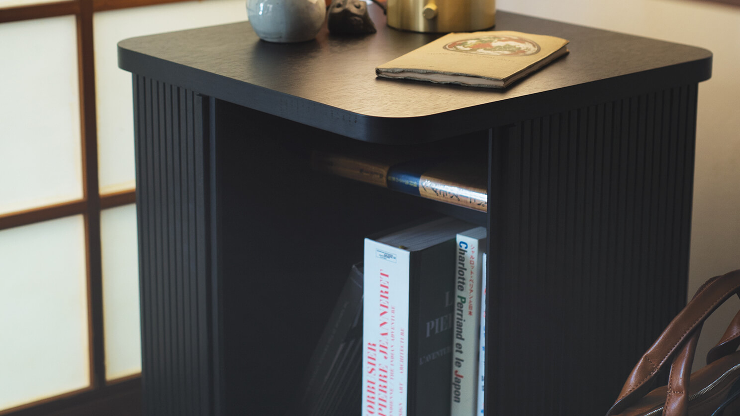 The Tambour modern side table in black filled with books and stacked with a notebook and vases